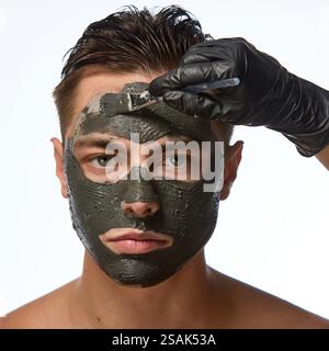 Man with smooth skin looking directly forward, and hand wearing black glove holding brush, mask covering most of face against white studio background. Stock Photo