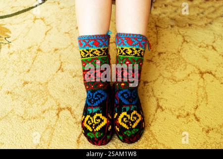 Beautiful wool socks made of multicolored threads on the girl's feet. Stock Photo