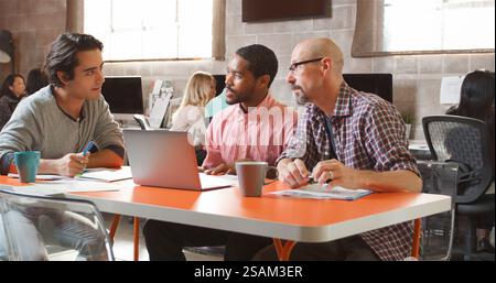 Three Designers In Creative Business Using Laptop Meeting In Modern Multi-Cultural Office Stock Photo