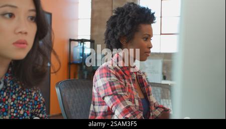Close Up Of Two Female Designers At Desks Working On Computers Talking Together In Modern Office Stock Photo