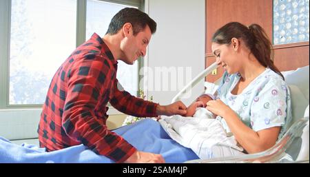 Loving Parents With Newborn Baby Boy Lying In Hospital Bed Stock Photo