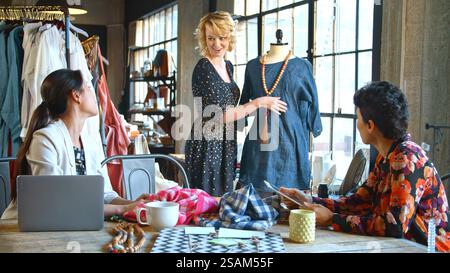 Three Female Fashion Designers In Studio Meeting Discussing Garment On Dummy Stock Photo