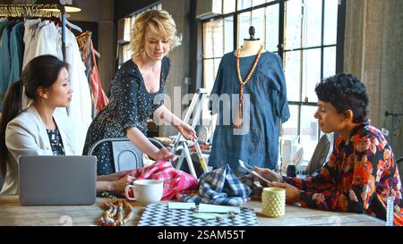 Three Female Fashion Designers In Studio Meeting Discussing Garment On Dummy Stock Photo