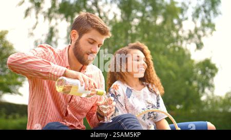 Young Couple Outdoors In Countryside Having Picnic With Man Pouring Glass Of Wine Stock Photo