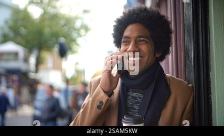 Stylish Young Man With Takeaway Coffee Making Phone Call On City Street Using Mobile Phone Stock Photo