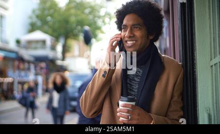 Stylish Young Man With Takeaway Coffee Making Phone Call On City Street Using Mobile Phone Stock Photo