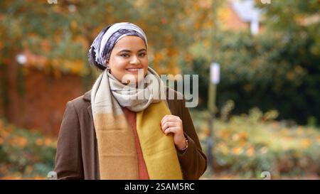 Portrait Of Smiling Young British Muslim Woman Wearing Headscarf In Autumn Park Stock Photo
