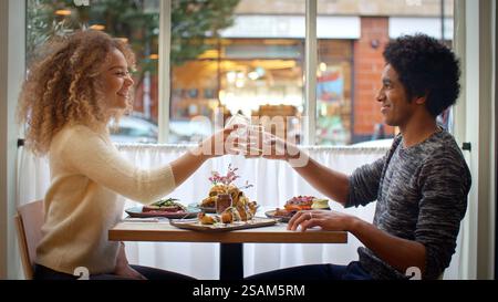Young Couple Doing Cheers With Drinks Enjoying Meal On Date In City Restaurant Together Stock Photo