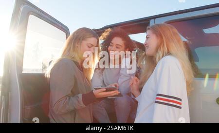 Group Of Young Female Friends On Road Trip Planning Journey Sitting In Car With Digital Tablet Stock Photo