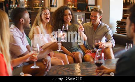 Group Of Multi-Cultural Young Friends Sitting In Bar Or Vineyard Tasting And Drinking Wine Together Stock Photo