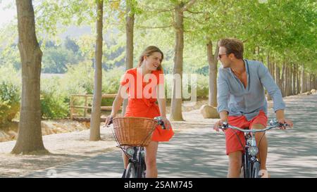 Young Couple Cycling Along Tree Lined Country Road In Summer Stock Photo