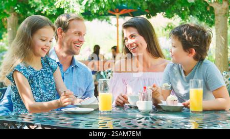 Family Sitting At Table Enjoying Snack At Outdoor Cafe Or Restaurant Stock Photo