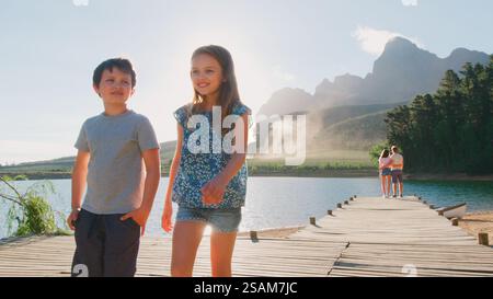 Family On Vacation Standing On Wooden Jetty By Lake With Mountains In Background Stock Photo