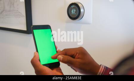 Close Up Of Man Setting Smart Heating Thermostat Using Green Screen Mobile Phone App Stock Photo