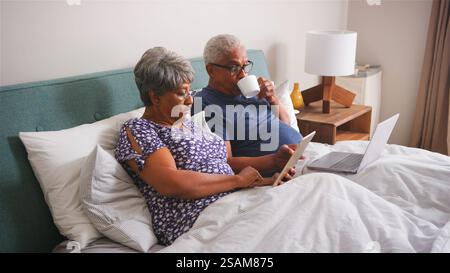 Senior Couple Lying In Bed At Home Using Digital Devices Stock Photo