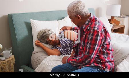 Senior Man Comforting Woman With Depression Lying In Bed At Home Stock Photo