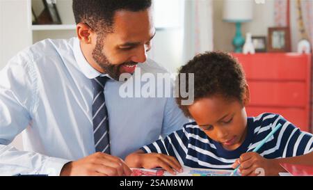 Father With Son Sitting At Desk In Bedroom At Home Colouring In Picture Stock Photo
