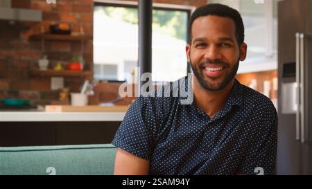 Portrait Of Smiling Young Man Relaxing On Sofa At Home Stock Photo