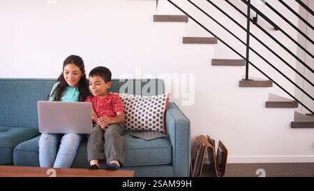 Brother And Sister Sitting On Sofa At Home Using Laptop Computer Together Stock Photo