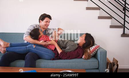 Family Shot With Parents Lying On Sofa And Playing With Son At Home Stock Photo