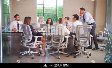 Business Team Meeting Sitting Around Table In Modern Office Discussing Documents Stock Photo