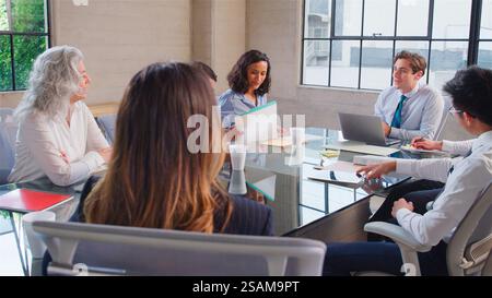 Business Team Meeting Sitting Around Table In Modern Office Discussing Documents Stock Photo