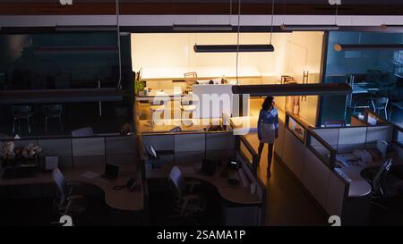 Wide Angle Shot Of Businesswoman Working Late At Night Standing In Empty Office Stock Photo