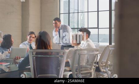 Business Team Meeting Sitting Around Table In Modern Office Discussing Documents Stock Photo