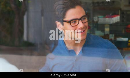 View Through Window Of Smiling Young Man Meeting Friends In Coffee Shop Stock Photo