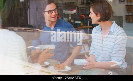 View Through Window Of Smiling Young Man Meeting Friends In Coffee Shop Stock Photo