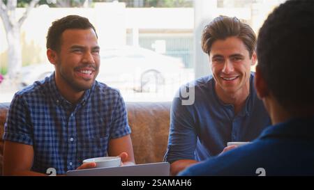 Group Of Businessmen Working At Laptop Sitting On Sofas In Coffee Shop Having Informal Meeting Stock Photo