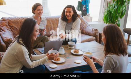 Group Of Businesswomen Working At Laptop Sitting On Sofas In Coffee Shop Having Informal Meeting Stock Photo