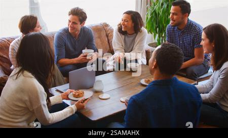 Group Of Businesspeople Working At Laptop Sitting On Sofas In Coffee Shop Having Informal Meeting Stock Photo