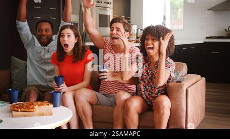 Excited Group Of Young Friends At Home Watching Sports On TV And Celebrating Together Stock Photo