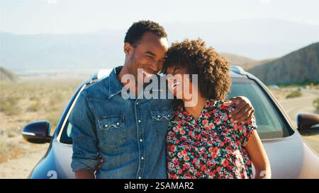 Smiling Young Couple On Road Trip Standing By Rental Car On Country Road Stock Photo