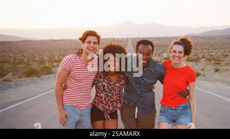Portrait Of Smiling Group Of Young Friends On Road Trip Standing On Country Road Stock Photo