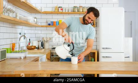 Young Man At Home Pouring Hot Water From Kettle Making Hot Drink In Modern Loft Apartment Stock Photo