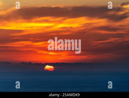 A breathtaking sunset over the ocean, with vibrant orange and yellow hues blending into the deep blue sea. Wispy clouds add texture to the sky as the Stock Photo