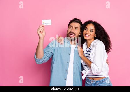 Young couple smiling while holding a credit card against a pink background Stock Photo