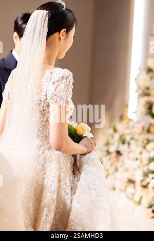 Bride is walking down the aisle with a bouquet of flowers. She is wearing a white dress and a veil Stock Photo