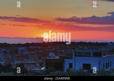 Sunset behind a town with a view of the sea and distant mountains, colourful sky in orange and blue, view of Zadar Dalmatia Croatia Stock Photo