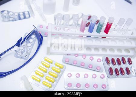 A variety of colorful pills and test tubes on a lab bench with safety glasses Stock Photo