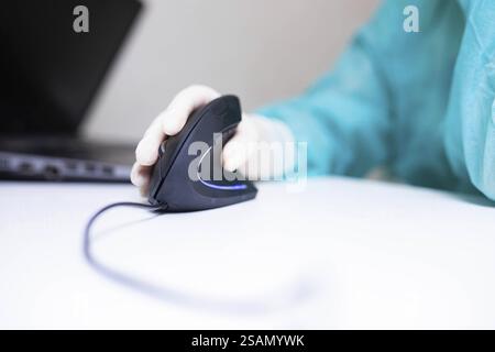 Gloved hand operating a computer mouse, with a laptop in the background Stock Photo