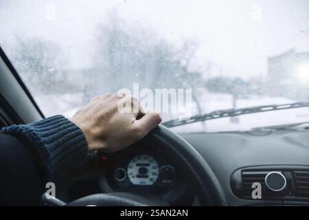 Hand on steering wheel looking out at frosted landscape through the windscreen Stock Photo