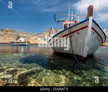Docked Fishing Boat isn the sunshine: A docked fishing boat in the crystal clear waters of the harbour at Cherronisos. Light bounces from the hull. Another boat is moore doff shore. Stock Photo