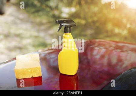 Yellow spray bottle and sponge on a sunlit glossy red car Stock Photo