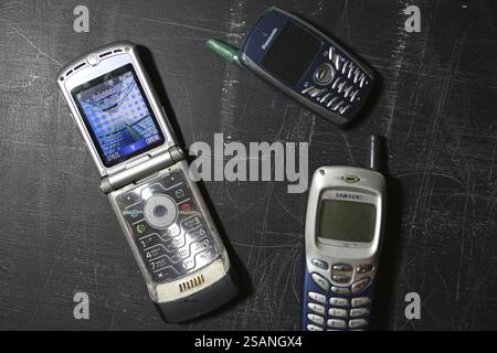 Three retro mobile phones including a Motorola flip phone on a black surface Stock Photo