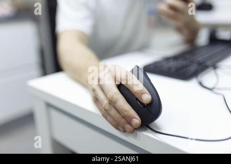 A hand using a computer mouse on a white desk near a keyboard Stock Photo
