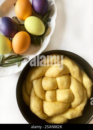 Easter sweet bread, cozonac or tsoureki and colorful Easter eggs on a white wooden table. Braided brioche, festive traditional dessert. Easter holiday. Stock Photo