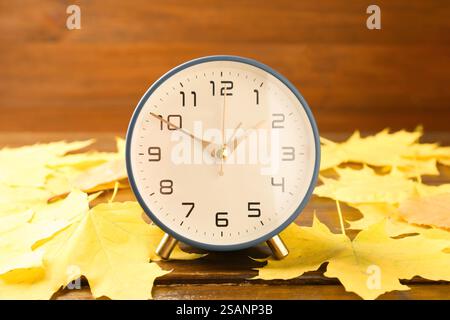 Autumn time. Alarm clock among leaves on wooden table, closeup Stock Photo